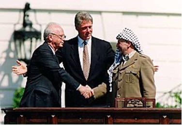 暫定自治政府原則の宣言 調印後に握手をするイスラエル・ラビン首相とPLOアラファト議長。中央は仲介したビル・クリントン米大統領（ウィキペディアより）